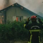 Vue aérienne d'un vaste incendie de forêt en Gironde, avec des flammes intenses et d'épais panaches de fumée s'élevant au-dessus des pins, des véhicules de pompiers au sol et des habitants évacuant.