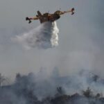 Vue aérienne d'un Canadair larguant de l'eau sur un feu de forêt dévastateur dans les Pyrénées-Orientales, avec une épaisse fumée s'élevant au-dessus des arbres calcinés.