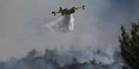 Vue aérienne d'un Canadair larguant de l'eau sur un feu de forêt dévastateur dans les Pyrénées-Orientales, avec une épaisse fumée s'élevant au-dessus des arbres calcinés.