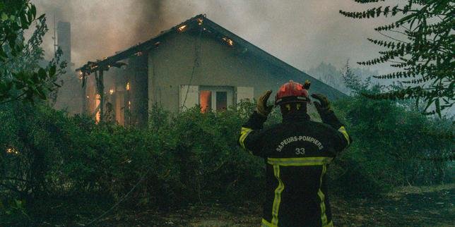 Vue aérienne d'un vaste incendie de forêt en Gironde, avec des flammes intenses et d'épais panaches de fumée s'élevant au-dessus des pins, des véhicules de pompiers au sol et des habitants évacuant.