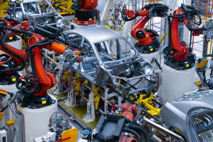Vue aérienne d'une usine automobile moderne au Maroc, avec des voitures neuves alignées et des camions de transport, symbolisant le succès de l'exportation.