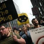 The New Luddites: Reclaiming Autonomy in a Hyper-Connected World 3 A diverse group of people gathered in Washington Square Park, some holding up 'dumbphones' or signs, listening to a speaker, symbolizing a movement against pervasive digital technology.