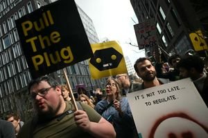 A diverse group of people gathered in Washington Square Park, some holding up 'dumbphones' or signs, listening to a speaker, symbolizing a movement against pervasive digital technology.
