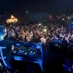 MOGA Essaouira 2026 : Dix Ans de Vagues Sonores et d'Électro Magique sur la Cité des Alizés 3 Vue aérienne du festival MOGA Essaouira avec des scènes de musique électronique en bord de mer et une foule dansante au coucher du soleil.