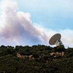 Smoke and flames surround large radio telescopes at NASA's Deep Space Communications Complex in Robledo de Chavela, Spain, amidst raging wildfires.