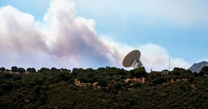 Smoke and flames surround large radio telescopes at NASA's Deep Space Communications Complex in Robledo de Chavela, Spain, amidst raging wildfires.