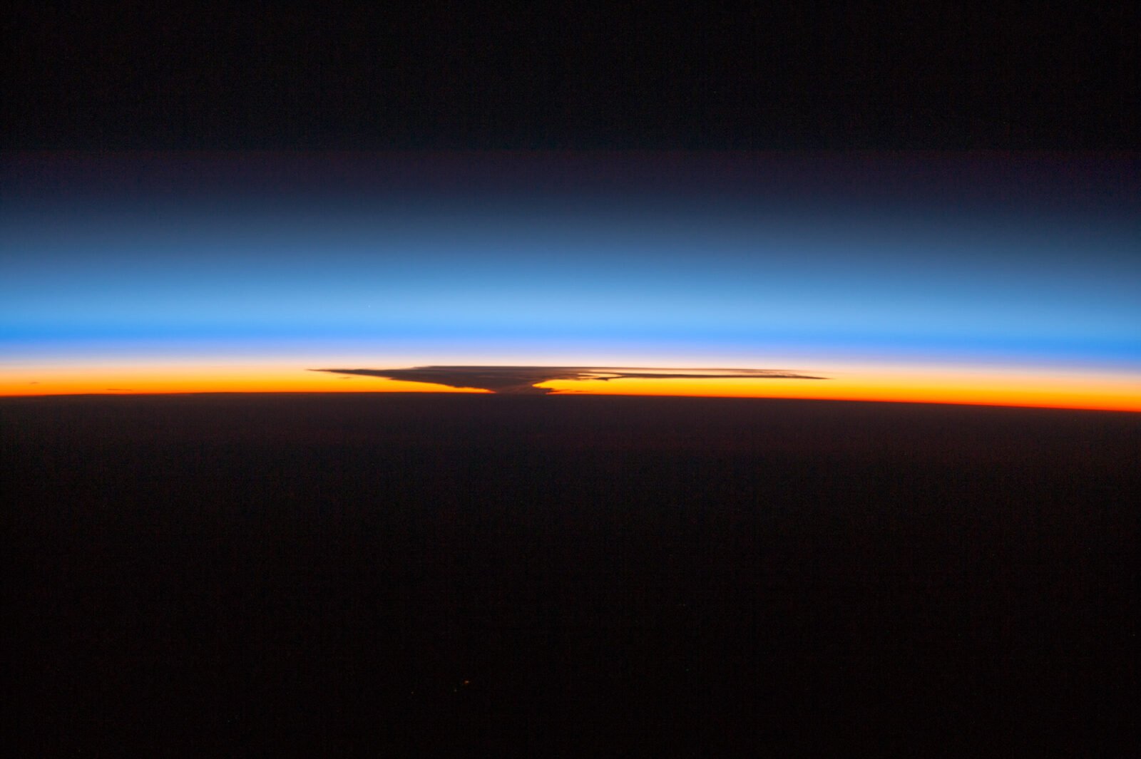 Astronauts aboard the ISS capture the Earth's ozone layer at sunset over Papua, New Guinea, with a thunderhead over Australia.