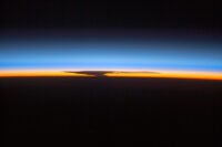 Astronauts aboard the ISS capture the Earth's ozone layer at sunset over Papua, New Guinea, with a thunderhead over Australia.