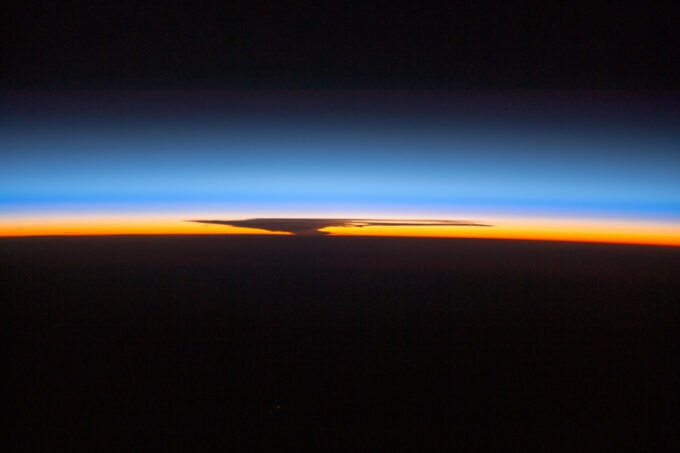 Astronauts aboard the ISS capture the Earth's ozone layer at sunset over Papua, New Guinea, with a thunderhead over Australia.