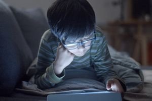 More Than Meets the Eye: The Systemic Health Risks of Screen Time 5 Person looking at a smartphone screen at night, with blue light emitting, illustrating the impact of screens on health.