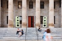 Seven-foot-tall sculptural speakers crafted from Baltic birch plywood and MDF mounted on the historic facade of the Village of Industry & Art building in Philadelphia, broadcasting music.