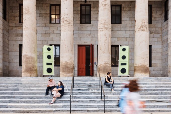 Seven-foot-tall sculptural speakers crafted from Baltic birch plywood and MDF mounted on the historic facade of the Village of Industry & Art building in Philadelphia, broadcasting music.