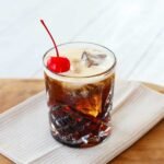 A freshly made Colorado Bulldog cocktail in a double old-fashioned glass, garnished with a maraschino cherry and ice.