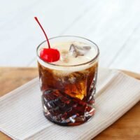 A freshly made Colorado Bulldog cocktail in a double old-fashioned glass, garnished with a maraschino cherry and ice.