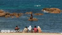 مهاجرون ينتظرون على الشاطئ في سبتة بإسبانيا، في 2 أغسطس/آب 2026