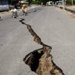صورة تظهر تشققات في الأرض أو مبان متضررة بعد زلزال في إندونيسيا، مع خلفية لجزيرة فلوريس.