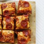 A square, golden-brown deep dish pizza with melted cheese, sauce, and toppings, cut into nine squares.