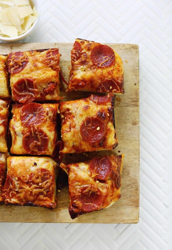 A square, golden-brown deep dish pizza with melted cheese, sauce, and toppings, cut into nine squares.