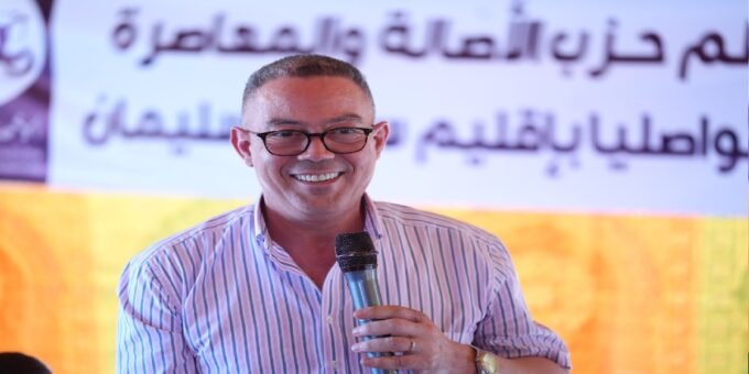 Fouzi Lekjaa s'adressant à la foule lors d'un rassemblement politique du PAM à Sidi Slimane, avec d'autres dirigeants du parti en arrière-plan.