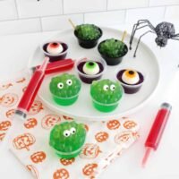 A collection of vibrant Halloween-themed jello shots, including witch's cauldron, monster, eyeball, and syringe designs, ready for a party.