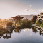 Exterior view of Hotel Chalet Mirabell nestled in the South Tyrolean Alps with a natural swimming pond and lush green lawns.