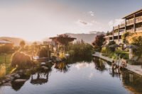 Exterior view of Hotel Chalet Mirabell nestled in the South Tyrolean Alps with a natural swimming pond and lush green lawns.