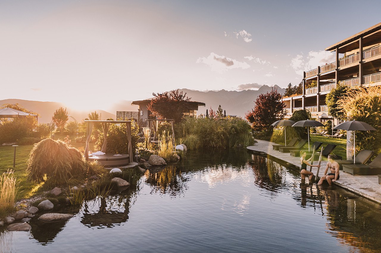 Exterior view of Hotel Chalet Mirabell nestled in the South Tyrolean Alps with a natural swimming pond and lush green lawns.