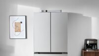 Jackery FridgeGuard, a sleek silver ultra-slim smart battery, standing next to a stainless steel refrigerator in a modern kitchen.