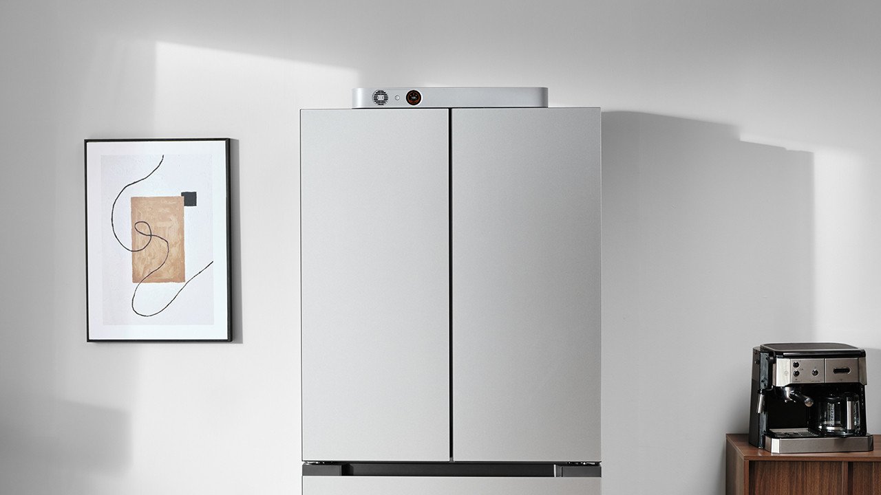 Jackery FridgeGuard, a sleek silver ultra-slim smart battery, standing next to a stainless steel refrigerator in a modern kitchen.