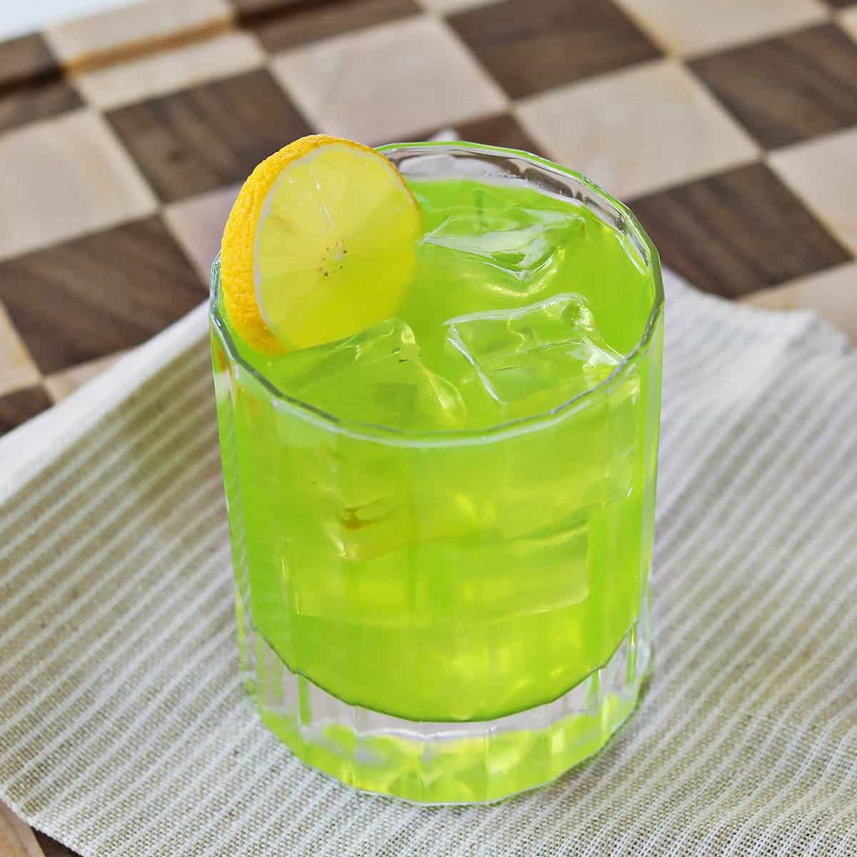 Neon Nostalgia: Shake Up the Perfect Midori Sour 3 A vibrant green Midori Sour cocktail garnished with a lemon wheel, served in a tall Collins glass with ice.