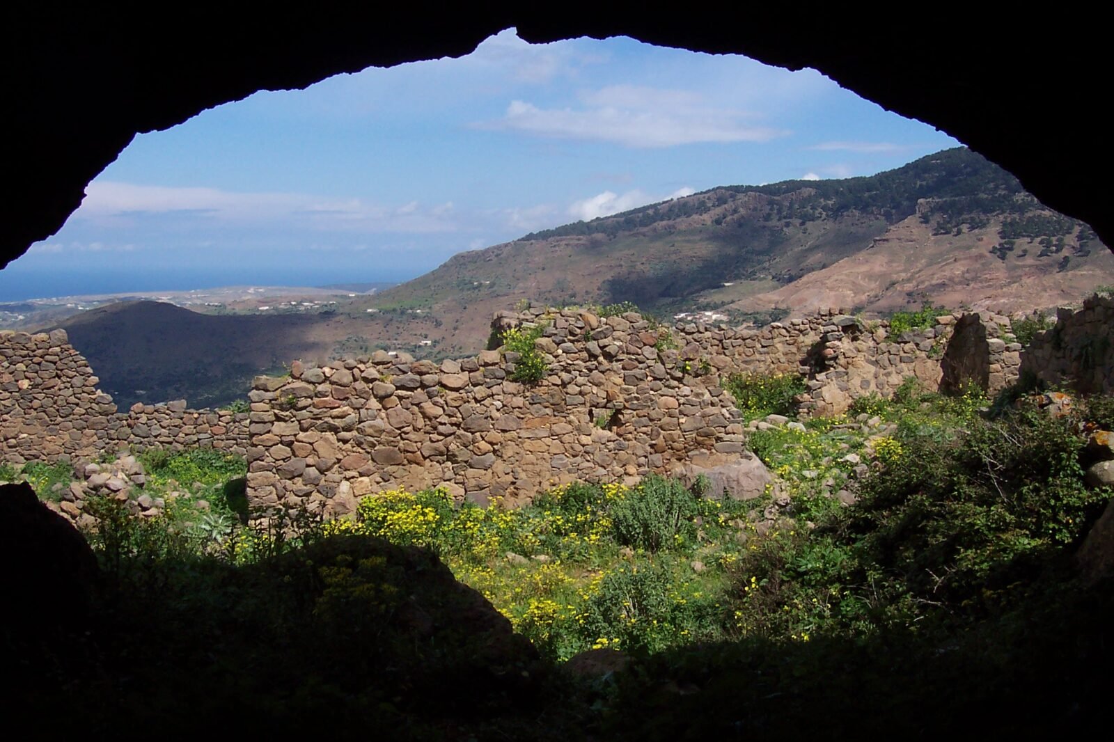 Vue panoramique du mont Gourougou, un ancien volcan près de Nador, avec ses falaises verdoyantes et des vestiges de tours en pierre au sommet, sous un ciel clair.