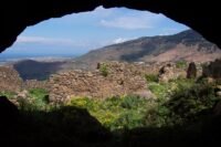 Vue panoramique du mont Gourougou, un ancien volcan près de Nador, avec ses falaises verdoyantes et des vestiges de tours en pierre au sommet, sous un ciel clair.