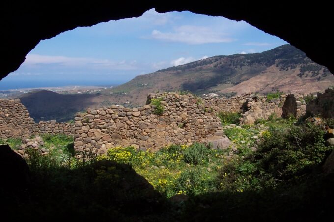 Vue panoramique du mont Gourougou, un ancien volcan près de Nador, avec ses falaises verdoyantes et des vestiges de tours en pierre au sommet, sous un ciel clair.