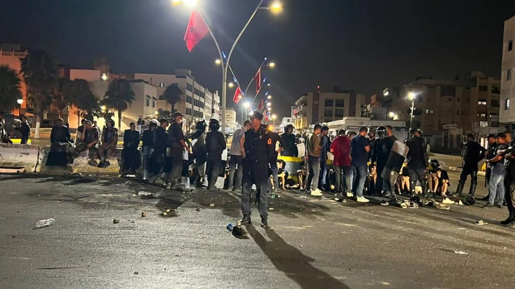 Vue aérienne de la clôture frontalière entre Nador, Maroc, et Melilla, Espagne, avec des silhouettes de personnes tentant de franchir la barrière.