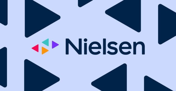 A person wearing a smartwatch, with a TV screen displaying streaming content in the background, symbolizing Nielsen's new measurement approach.