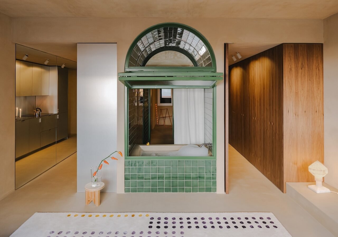 A modern, open-plan apartment in Barcelona featuring a central, arched bathtub integrated into the living space, designed by SIGLA Studio.