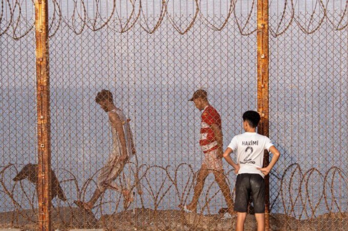 Des migrants, incluant femmes, hommes et enfants, tentent de franchir la frontière de Sebta, illustrant les défis de la mobilité humaine entre l'Afrique et l'Europe.