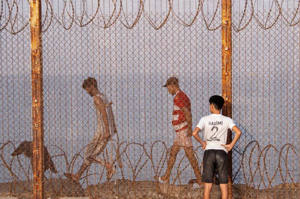 Des migrants, incluant femmes, hommes et enfants, tentent de franchir la frontière de Sebta, illustrant les défis de la mobilité humaine entre l'Afrique et l'Europe.