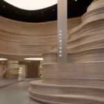 Interior view of SKIN1004's SoHo flagship store, showcasing the sinuous, layered wood 'Nature Wall' and reflective 'Mirror Wall' creating an expansive, natural valley-inspired landscape.