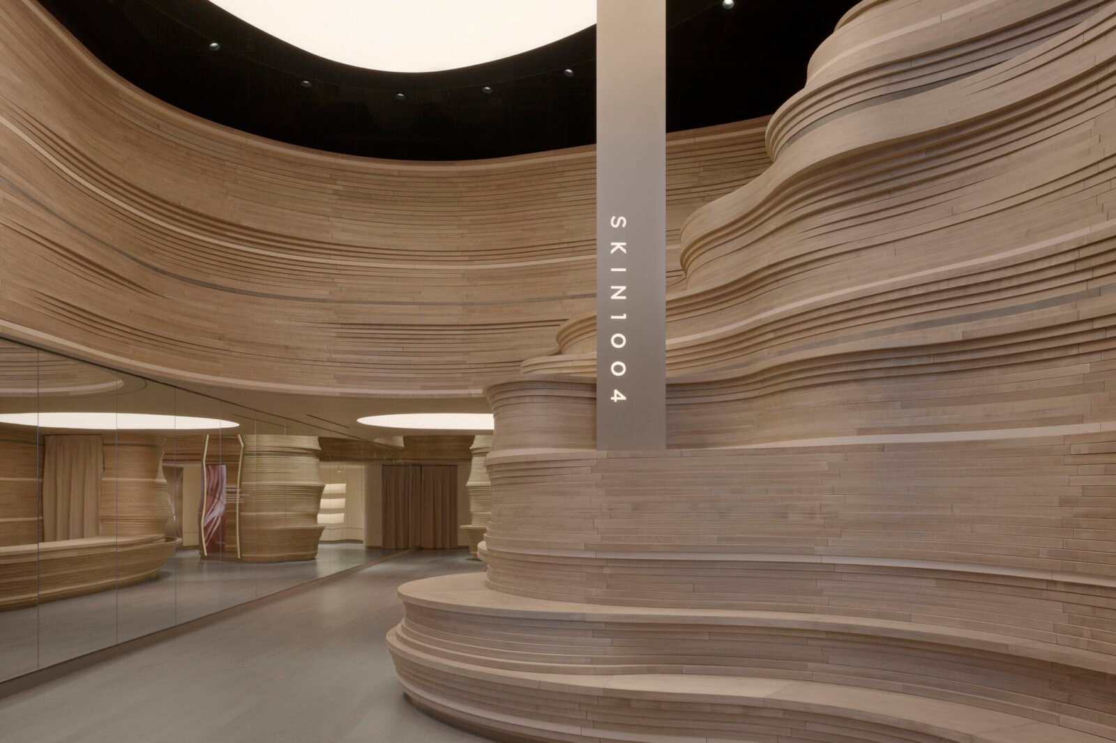 Interior view of SKIN1004's SoHo flagship store, showcasing the sinuous, layered wood 'Nature Wall' and reflective 'Mirror Wall' creating an expansive, natural valley-inspired landscape.