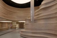 Interior view of SKIN1004's SoHo flagship store, showcasing the sinuous, layered wood 'Nature Wall' and reflective 'Mirror Wall' creating an expansive, natural valley-inspired landscape.