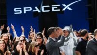 Elon Musk in front of a SpaceX Starship rocket, symbolizing the company's future ambitions and current market challenges.