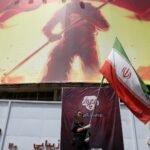 Iranian flag waving in Tehran amidst ongoing tensions with the U.S. near a giant banner