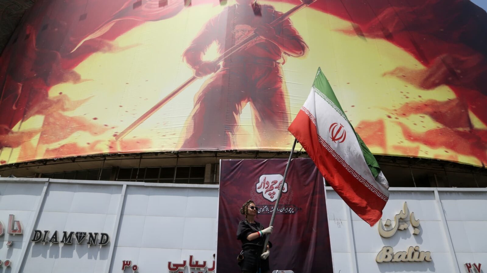 Iranian flag waving in Tehran amidst ongoing tensions with the U.S. near a giant banner