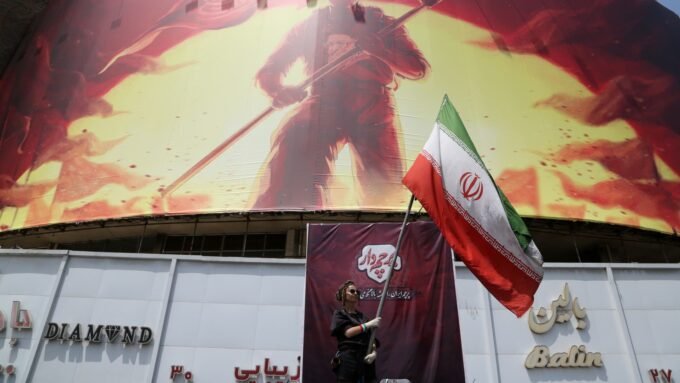Iranian flag waving in Tehran amidst ongoing tensions with the U.S. near a giant banner