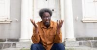 W. Kamau Bell, comedian and activist, holding a smartphone charger, representing his most indispensable tool.