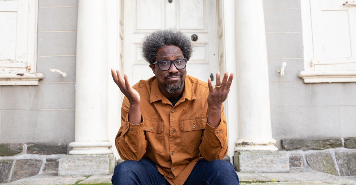 W. Kamau Bell, comedian and activist, holding a smartphone charger, representing his most indispensable tool.