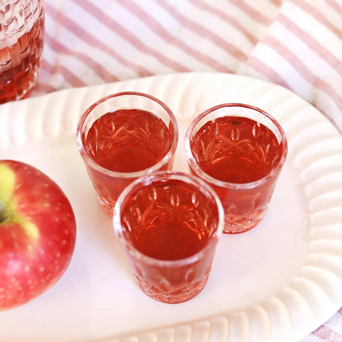 A vibrant red Washington Apple Shot in a clear shot glass, garnished with a thin apple slice, on a dark background.