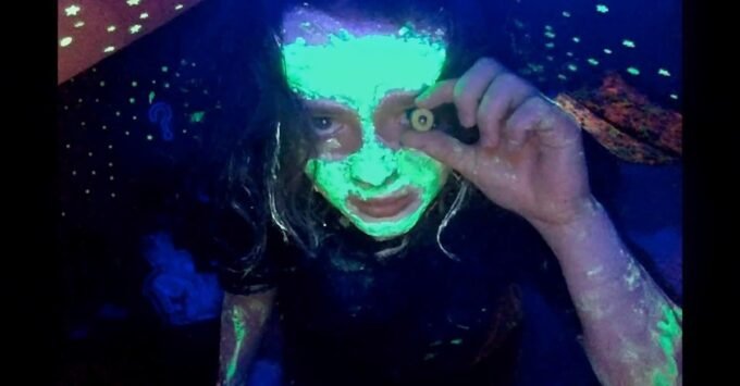 Still from 'We’re All Going to the World’s Fair' showing a young girl staring intensely into a webcam, bathed in screen light.