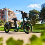 Veo's Rover electric trike, featuring three wheels, a cushioned seat, and baskets, in an urban setting.